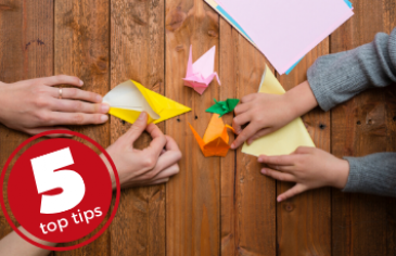 5 top tips origami to make, parent and child folding origami birds with brightly coloured paper on a wooden table