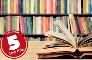 5 top tips: young adult authors to read. An open book on a table in front of a library shelf of multi-colour books