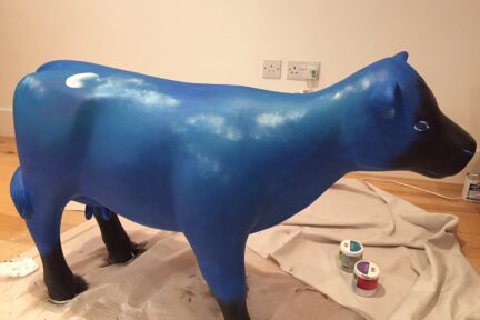 Museum of Cambridge mini-moo, mid-creation by artist Marlis Horgan, showing the night sky painted onto the cow.