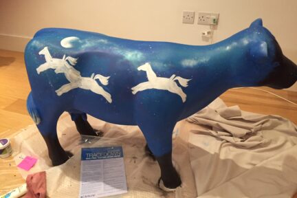 Museum of Cambridge mini-moo, mid-creation by artist Marlis Horgan, showing the night sky painted onto the cow with the rocking horse outlines in position.